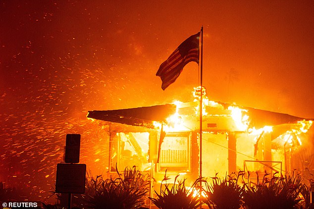 U.S. flag flies as fire engulfs structure as Palisades Fire burns during wind storm