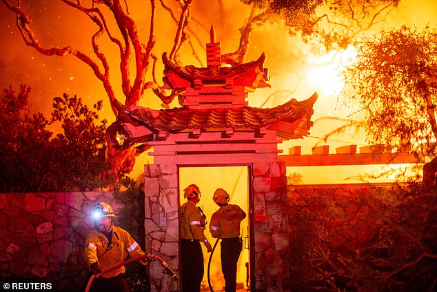 Firefighters battle the Palisades Fire as it burns during a storm on the west side of Los Angeles