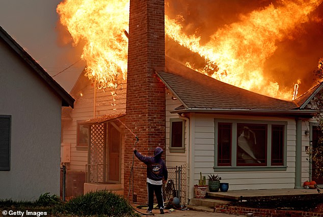 A person uses a garden hose yesterday in an attempt to save a house from becoming stuck in Altadena