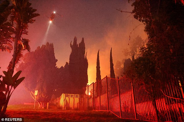 A helicopter flies as smoke rises from the Sunset Fire in the hills above Hollywood yesterday