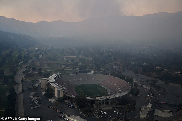 An aerial image shows smoke covering the slopes behind the Rose Bowl stadium due to wildfires, including the Eaton Fire, at dusk over Pasadena.