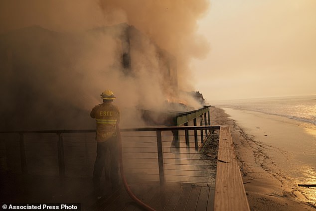 A firefighter protects a beachfront property while battling the Palisades Fire on Thursday.