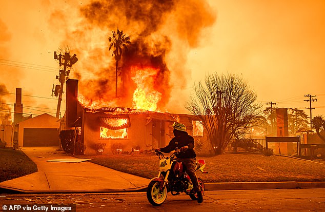 A motorcyclist stops to look at a burning house during the Eaton fire.