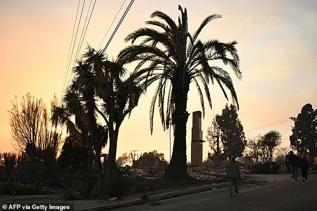 Residents are photographed walking past a burned home after searching their home for belongings during the Palisades Fire in Pacific Palisades on Thursday.