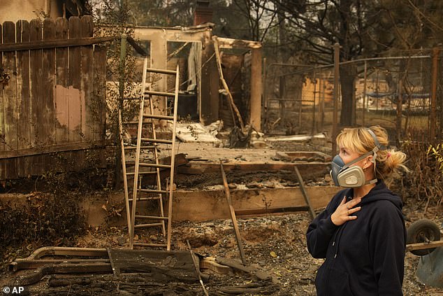 A woman looks at the charred remains of her neighborhood, wearing a mask because of the heavy smoke