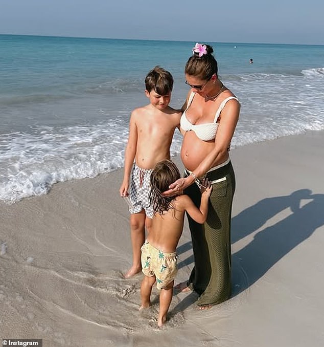 Her two eldest children sweetly gazed at her growing stomach in one picture as they enjoyed a family day at the beach ahead of the new arrival.