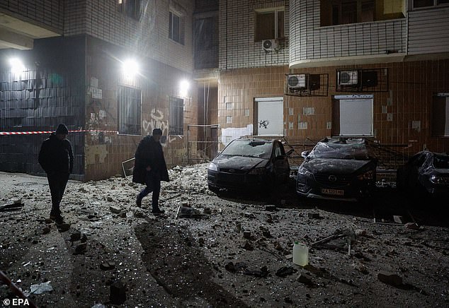 Local people walk near damaged cars at the site where debris from a drone fell on a residential building, in kyiv, Ukraine, January 10, 2025.