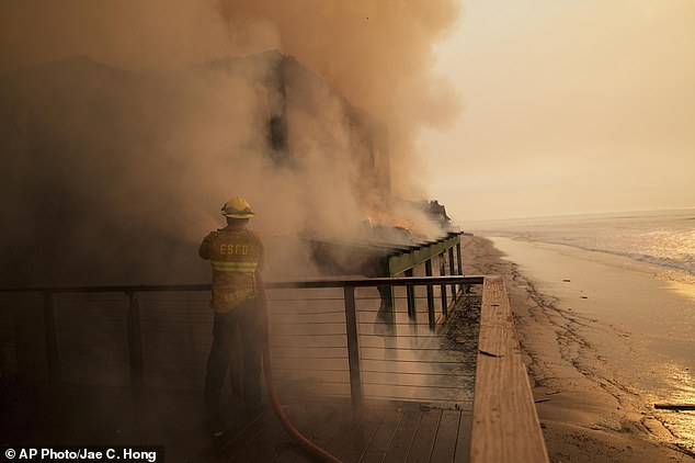 A firefighter protects a beachfront property while battling the Palisades Fire on Thursday, January 9, 2025 in Malibu, California