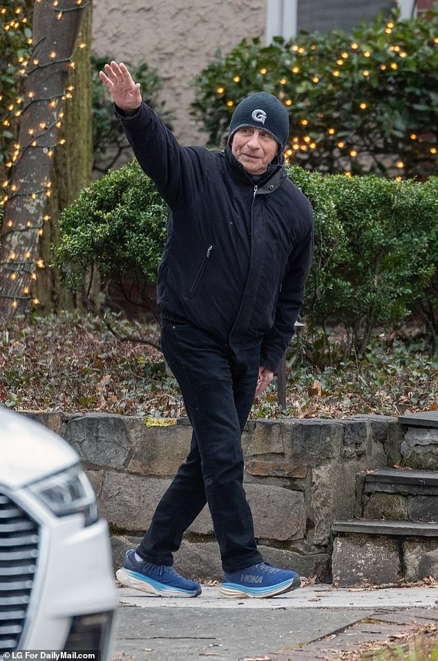 Fauci waves to the driver who is standing across the street and is part of security