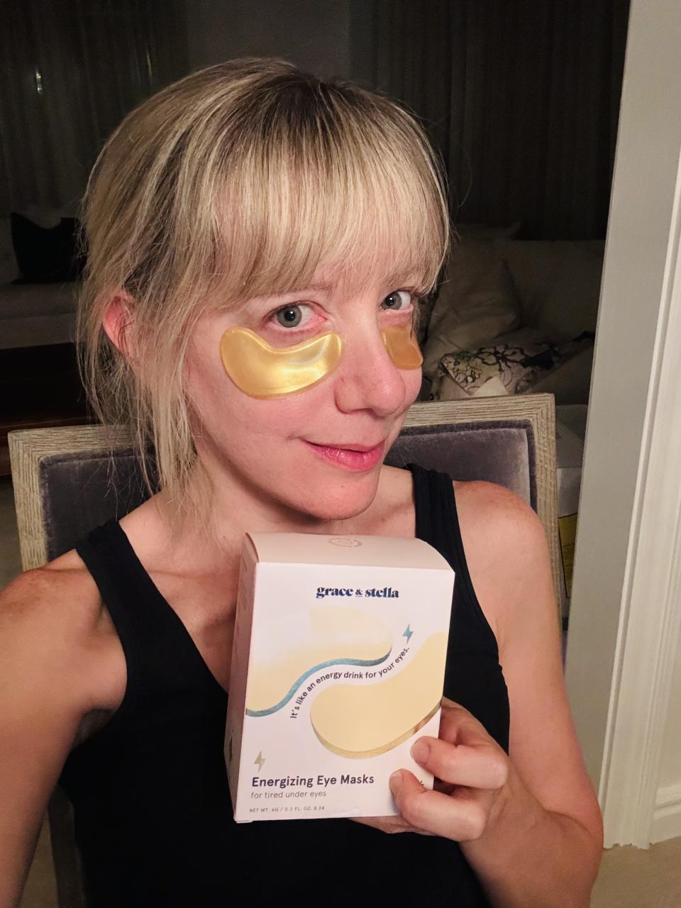 Blonde woman holding a box and wearing gold Grace and Stella under eye masks.